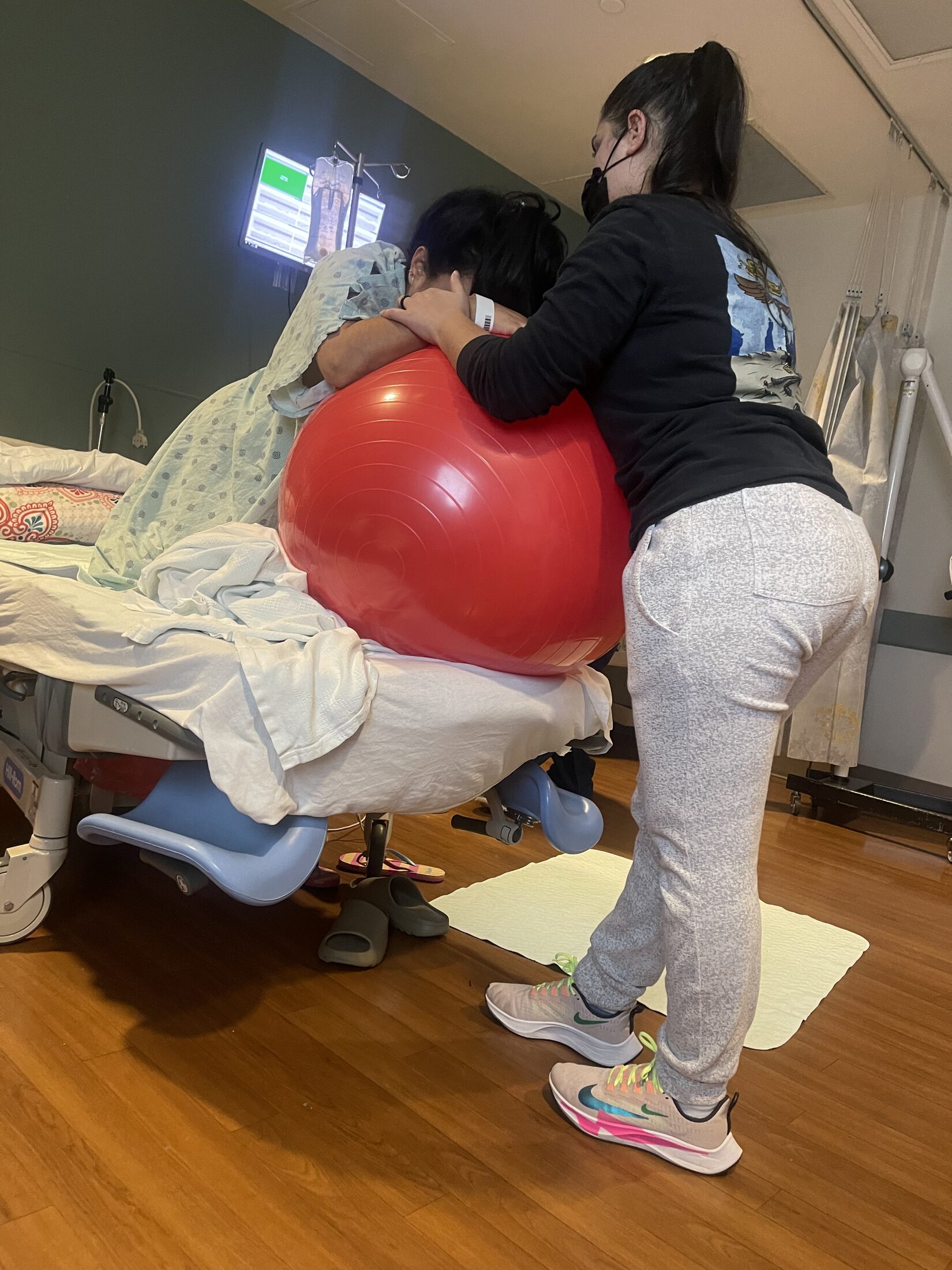 Doula supporting a laboring mother leaning over a birth ball